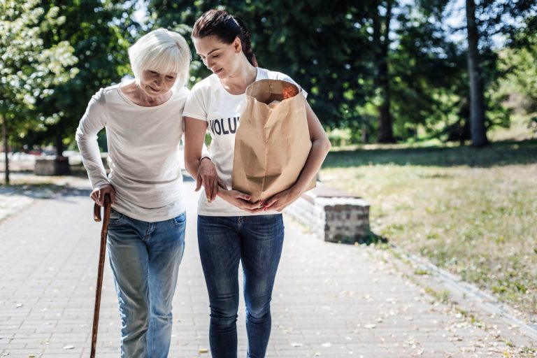 Femme âgée handicapée aidant par une jeune dame pour porter courses